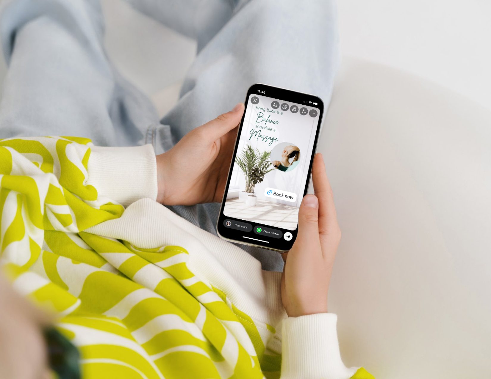 A person in a green and white sweater, lounging on a sofa with their phone in their hand. the phone shows an Instagram Story that says Bring Back the Balance, Schedule a Massage and has a link to their online booking.